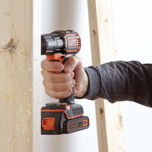 BLACK+DECKER ASD184K cordless drill in use, drilling into wood, side view, visible 18V lithium battery.