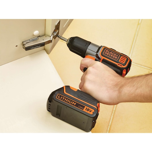 BLACK+DECKER ASD18KB cordless drill used to fasten a hinge, black and orange, close-up photo.