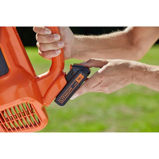 Close-up photo of BLACKDECKER BCBL200B leaf blower with hand inserting 18V lithium battery outdoors.