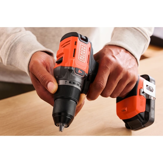 Person holding a BLACK+DECKER cordless drill on a wooden surface, showing the tool's details and design.