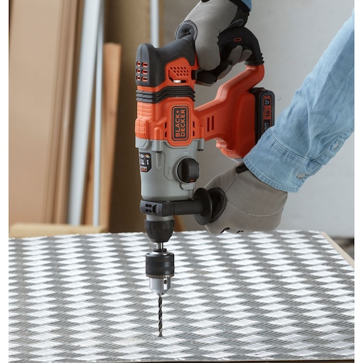 BLACK+DECKER BCD900B cordless hammer drill in use on patterned metal surface, close-up view.