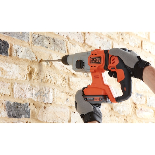 Photo of BLACKDECKER BCD900E2K cordless hammer drill in use on a brick wall, orange and black color.