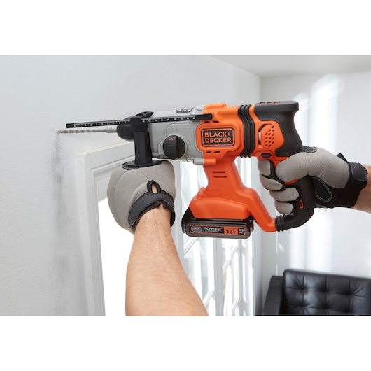 BLACK+DECKER BCD900E2K cordless hammer drill in use, orange and black, drilling wall near window.