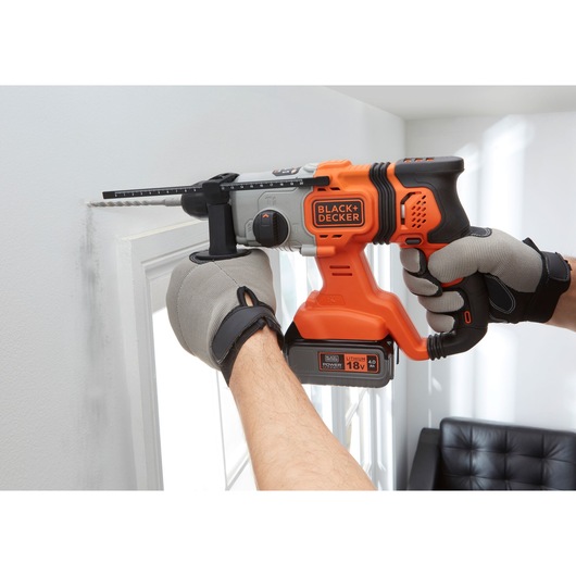 BLACK+DECKER BCD900M1K cordless hammer drill in use drilling into a white wall, visible 18V lithium battery.