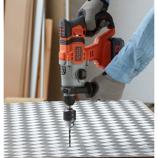 BLACK+DECKER BCD900M1K cordless hammer drill in use, drilling into a metal surface, side view.