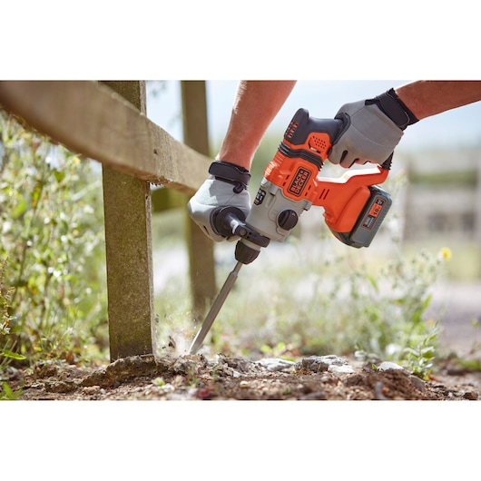 Photo of BLACKDECKER BCD900M1K rotary hammer drill used outdoors on concrete, gloved hands holding tool.