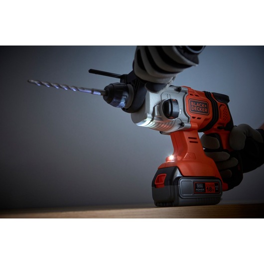 Photo of BLACK+DECKER BCD900M1K cordless hammer drill in use, orange and black design, side angle view.