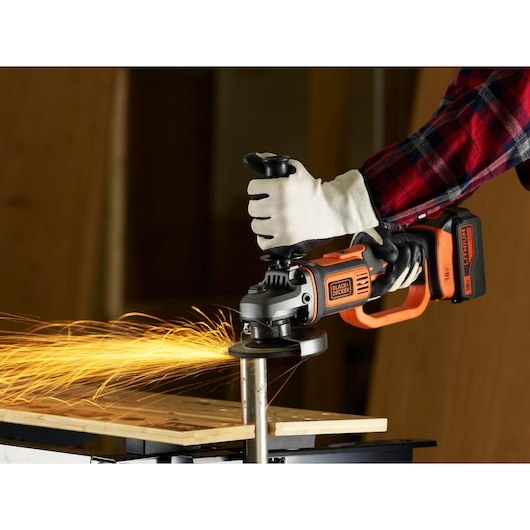 Photo of BLACKDECKER BCG720M1 cordless angle grinder in use, cutting metal pipe, with sparks flying.