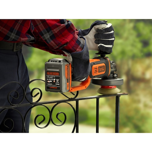 BLACKDECKER BCG720M1 cordless angle grinder used on metal railing outdoors, orange and black design.