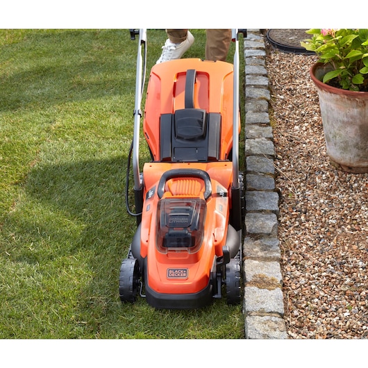 Photo of BLACKDECKER BCMW33182L2 lawn mower on grass near garden edge, top view.
