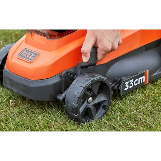 Photo of BLACK+DECKER BCMW33182L2 lawn mower wheel with adjustable height lever, close-up on grass.