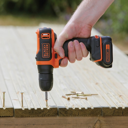 Photo of BLACKDECKER BDCD12K cordless drill driving a screw into wooden boards outdoors.