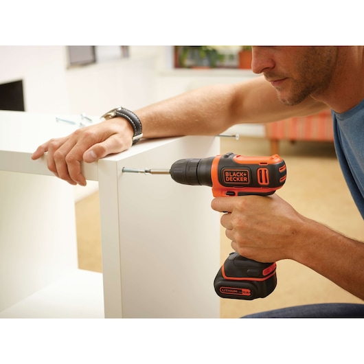 BLACKDECKER BDCD12 cordless drill in use assembling white furniture, close-up angle.