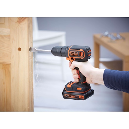 Photo of BLACKDECKER BDCD18 cordless drill in use, drilling into wood, orange and black design.