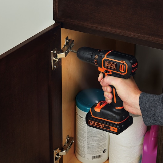 Photo of BLACKDECKER BDCDC18K1 cordless drill being used to tighten a hinge inside a wooden cabinet.