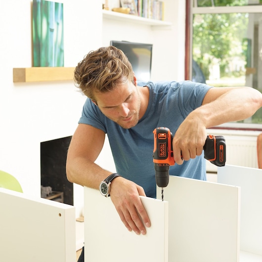 Photo of BLACKDECKER BDCDD12B cordless drill used for assembly on white furniture panel indoors.