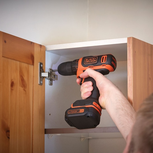 BLACKDECKER BDCDD12B cordless drill used to assemble a wooden cabinet, product held by hand.