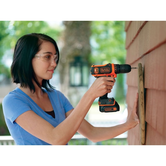 BLACKDECKER BDCDD12KB cordless drill used outdoors on a red wall, product category: photography.