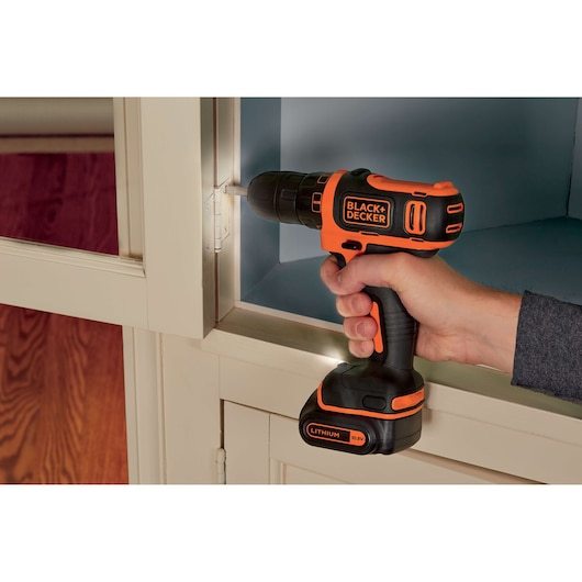 Photo of BLACKDECKER BDCDD12KB cordless drill being used on a cabinet hinge, orange and black design.