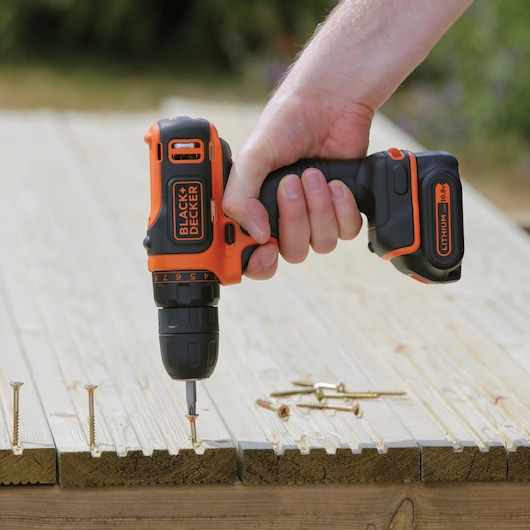 Photo of BLACK+DECKER BDCDD12KB cordless drill driving a screw into wood, visible lithium battery.