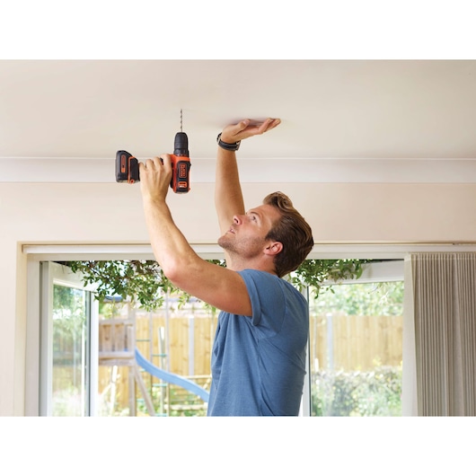 Photo of BLACKDECKER BDCDD12 cordless drill in use drilling into a ceiling indoors.