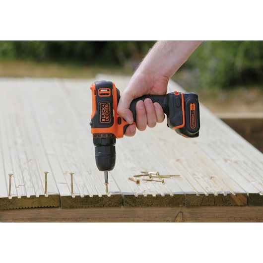 BLACKDECKER BDCDD12 cordless drill in use on wood with screws, close-up outdoor photography.
