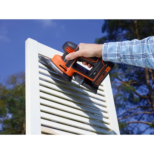 BLACKDECKER BDCDS18 cordless sander used on white shutter outdoors, orange and black tool held in hand.