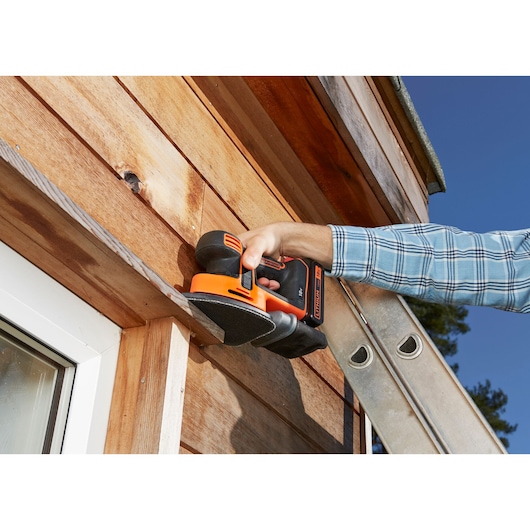 BLACKDECKER BDCDS18 cordless sander used on wooden exterior siding, close-up action scene.