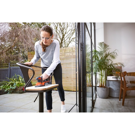 Photo of BLACKDECKER BDCDS18 sander used to sand a chair outdoors next to a patio door.