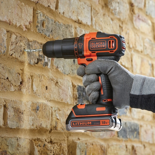 BLACK+DECKER BDCHD18K1B2 cordless drill in use drilling into a brick wall, close-up view.