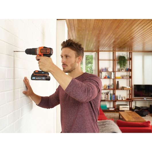 Photo of BLACKDECKER cordless drill BDCHD18KST drilling into a white brick wall in a modern living room.