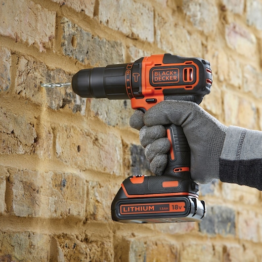 BLACKDECKER cordless drill BDCHD18K drilling into brick wall, orange and black, lithium 18V battery.