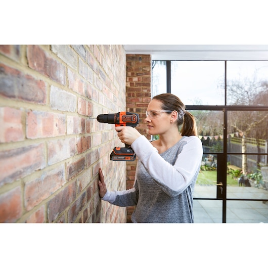 Photo of BLACKDECKER BDCHD18K cordless drill in use on brick wall, highlighted orange and black design.
