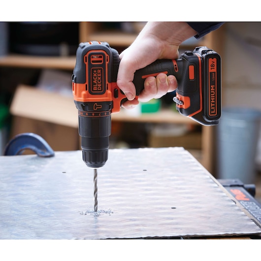 BLACKDECKER BDCHD18 cordless drill in use drilling metal, orange and black color, close-up side angle.