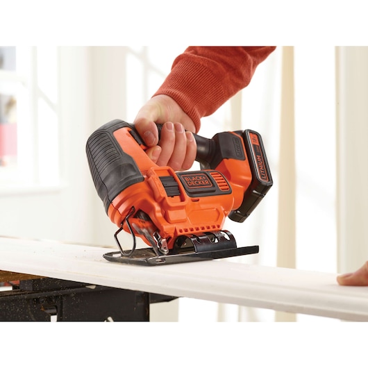Photo of BLACKDECKER BDCJS18 cordless jigsaw cutting wood, orange and black design, handheld tool.