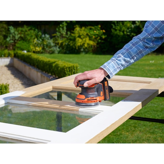 BLACKDECKER BDCROS18 cordless sander used on a wooden door outdoors, product in action.