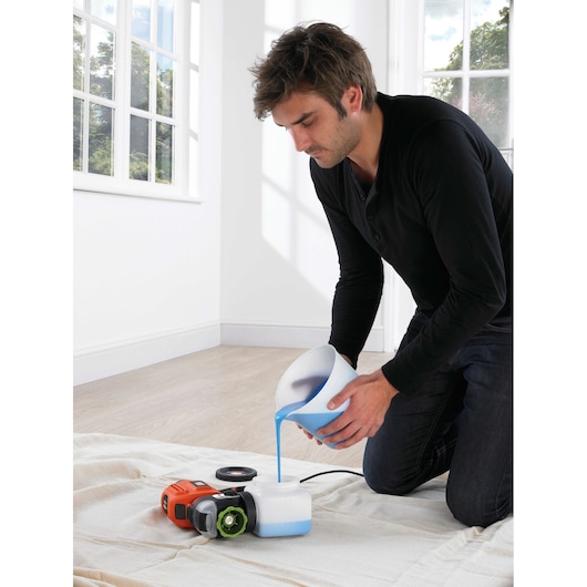 BLACKDECKER BDPS400 paint sprayer on floor, person pouring blue paint into container indoors.