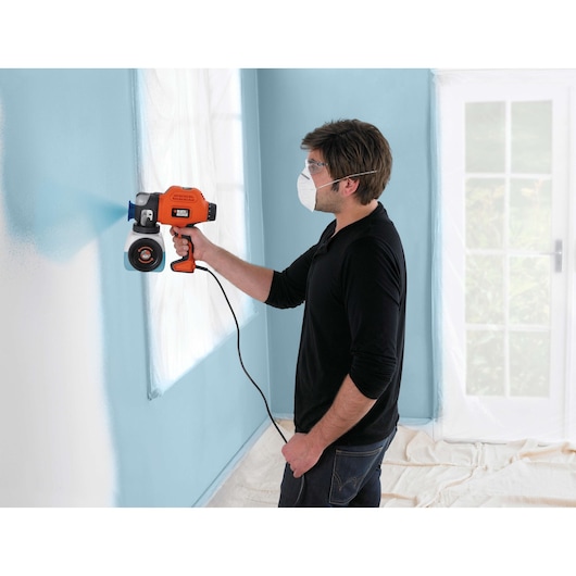 BLACKDECKER BDPS400 paint sprayer in use painting a light blue wall, product held by a person indoors.