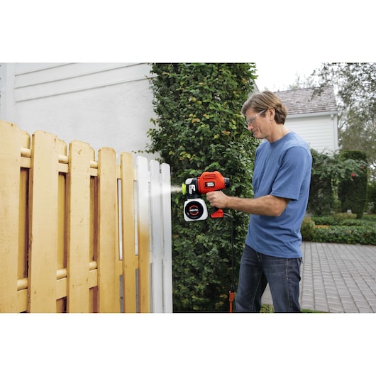 Photo of person using BLACK+DECKER BDPS600K paint sprayer on a wooden outdoor fence.