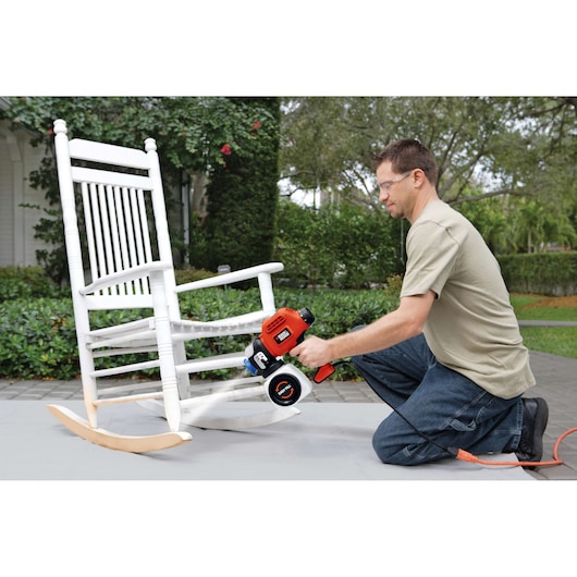 Photo of person using BLACKDECKER BDPS600K paint sprayer to repaint a white wooden rocking chair outdoors.