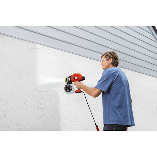 BLACKDECKER BDPS600K paint sprayer used on textured white wall, outdoor setting.