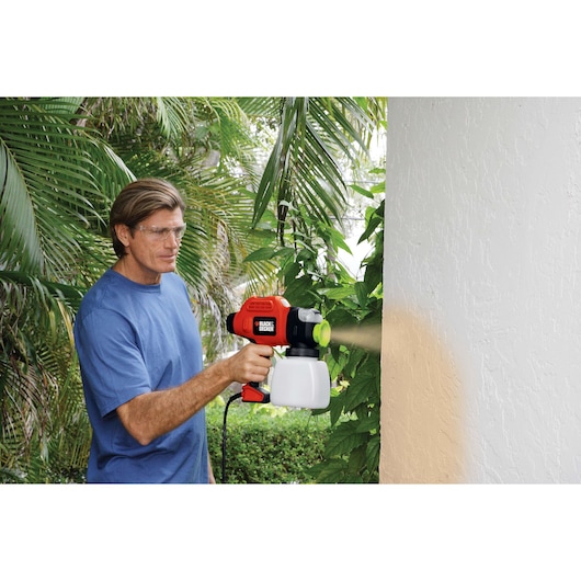 Photo of BLACKDECKER BDPS600K paint sprayer in use painting an exterior white wall outdoors.