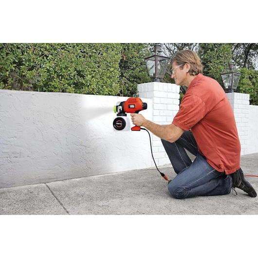 BLACKDECKER BDPS600K paint sprayer in use outdoors on a white wall.