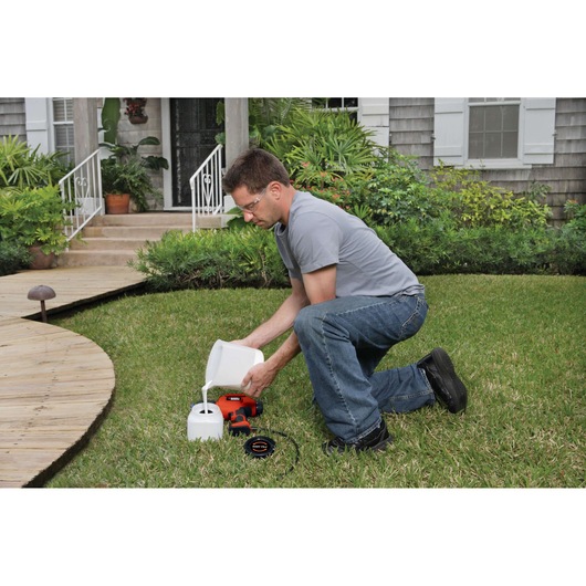 BLACKDECKER BDPS600K sprayer being filled with liquid on lawn, product and accessories visible.