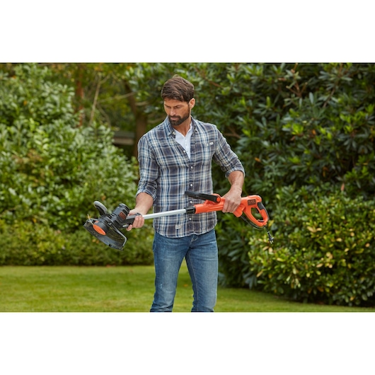 Photo of a person holding BLACKDECKER BESTE630CM orange and black string trimmer in a garden setting.