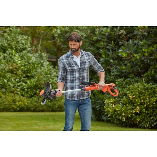 Person holding BLACKDECKER BESTE630CM orange and black grass trimmer in a garden.