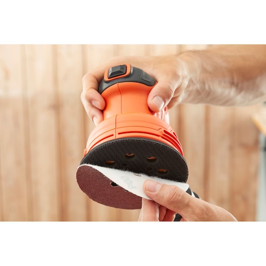 Photo of BLACKDECKER BEW210 random orbital sander with sandpaper disc being attached, close-up view.