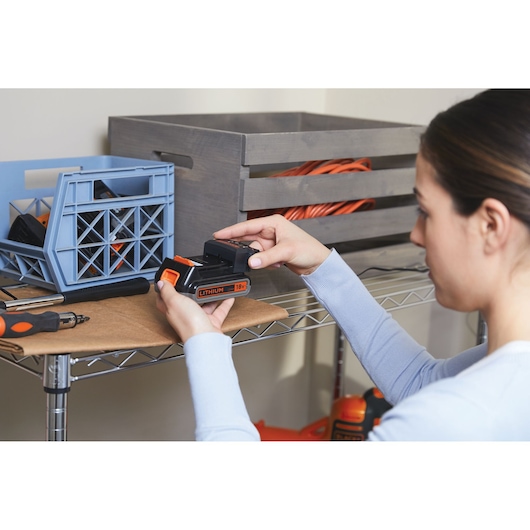 Photo of BLACKDECKER BHFEV182B 18V lithium battery in use, held by a person next to storage shelves.