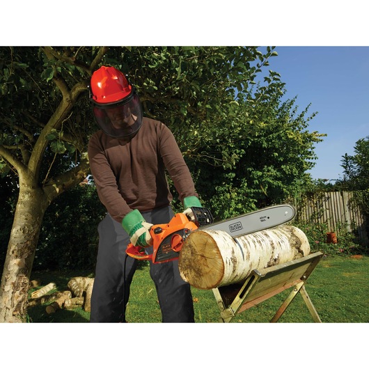 BLACKDECKER CS2040 chainsaw cutting log outdoors, held by person with safety gear, garden setting.