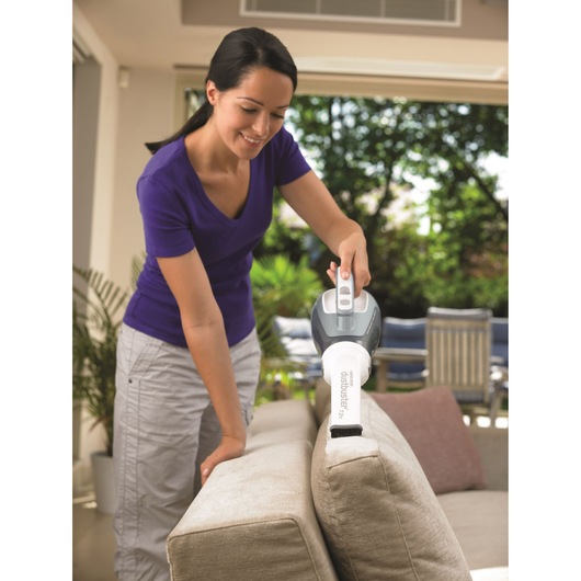 BLACKDECKER DV7210ECN handheld vacuum cleaner in use cleaning a beige sofa in a living room.